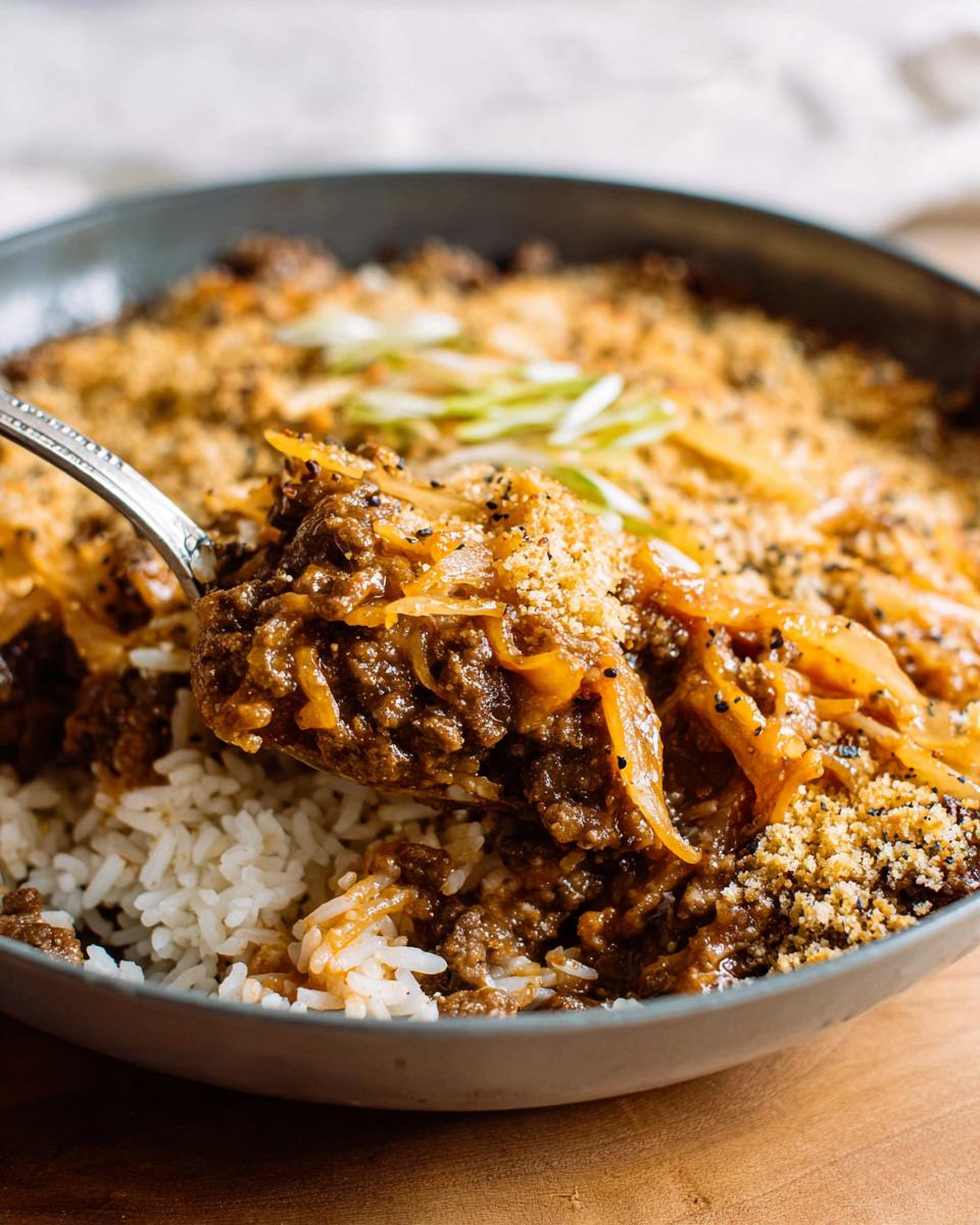 A spoonful of comforting ground beef recipe over white rice, topped with breadcrumbs and green onions.
