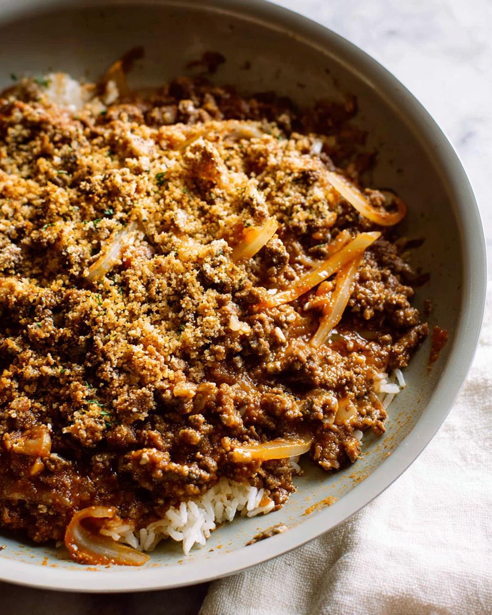 A close-up of a comforting ground beef recipe served over white rice, topped with a crunchy breadcrumb mixture and onions.