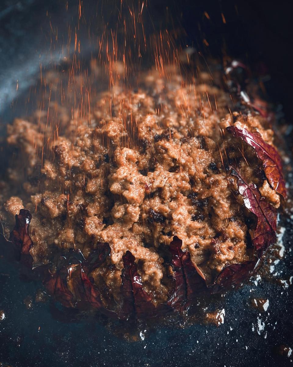 Close-up of ground beef cooking in a pan with dramatic sparks flying.
