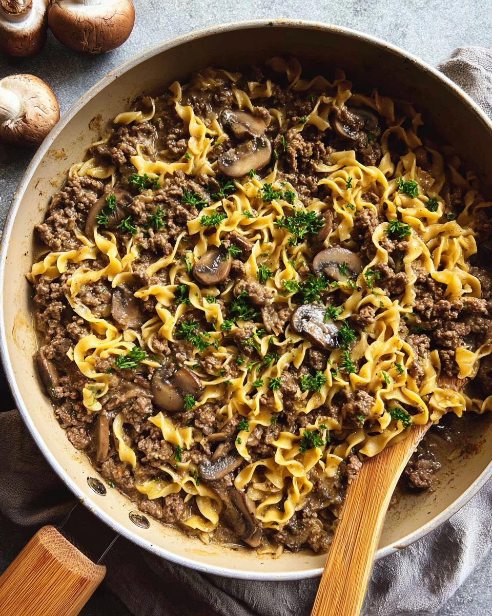 A close-up overhead view of a skillet filled with ground beef, egg noodles, mushrooms, and parsley, showcasing one of the easy ground beef recipes.