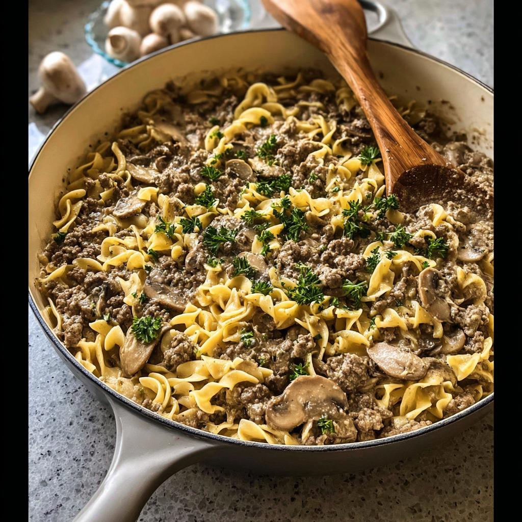 A close-up of a skillet filled with ground beef recipes made easy: creamy noodles, seasoned ground beef, and mushrooms, garnished with parsley.