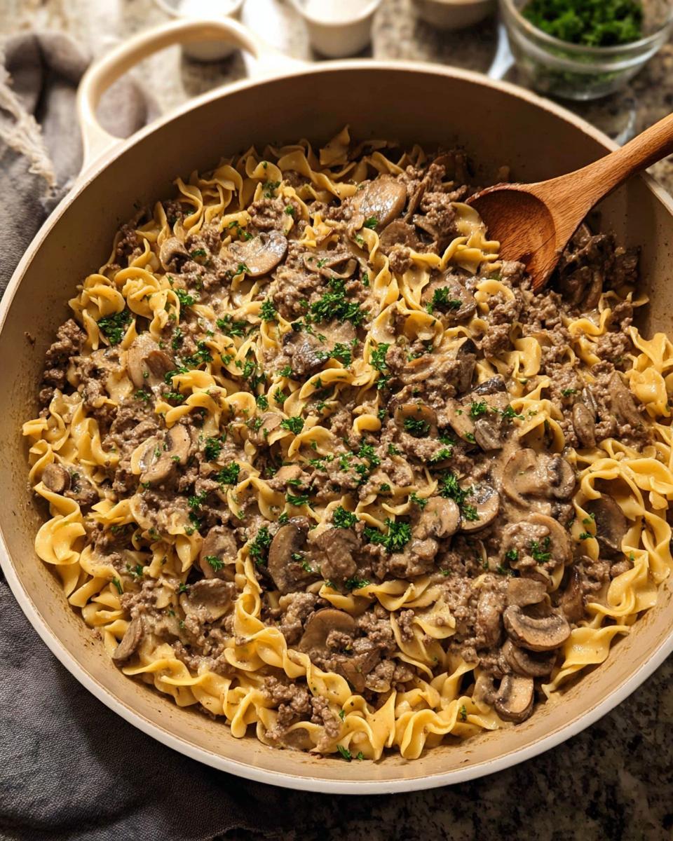 A hearty skillet dish featuring ground beef, egg noodles, and sliced mushrooms, garnished with parsley. A simple ground beef recipe.