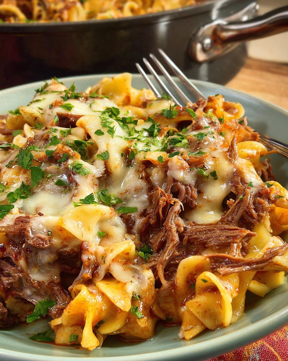 A close-up of a bowl of pasta with shredded beef and melted cheese, garnished with parsley. A classic dinner recipe with a twist.