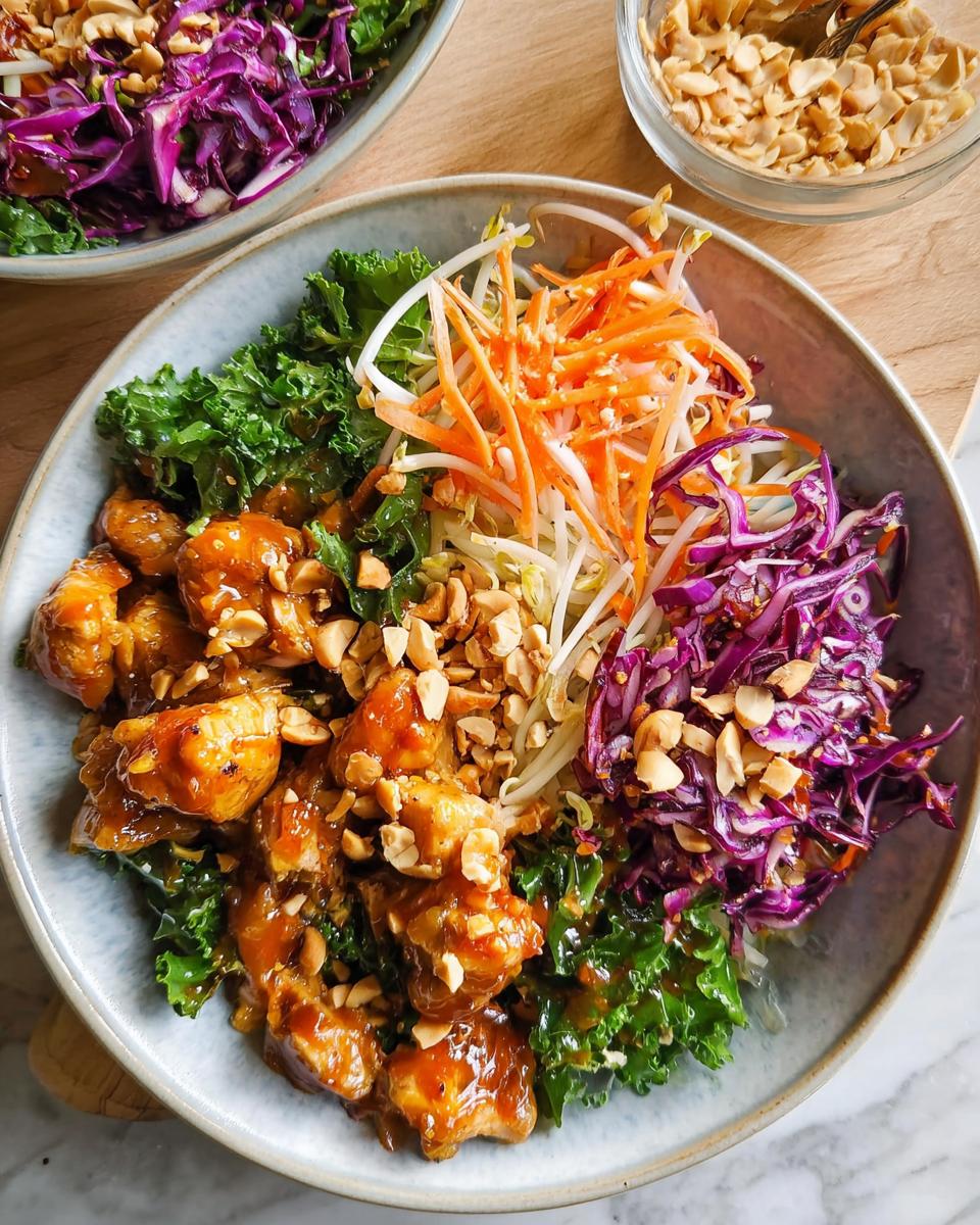 A vibrant bowl of Simple Chicken At Home with kale, shredded carrots, bean sprouts, and red cabbage, topped with chopped peanuts.