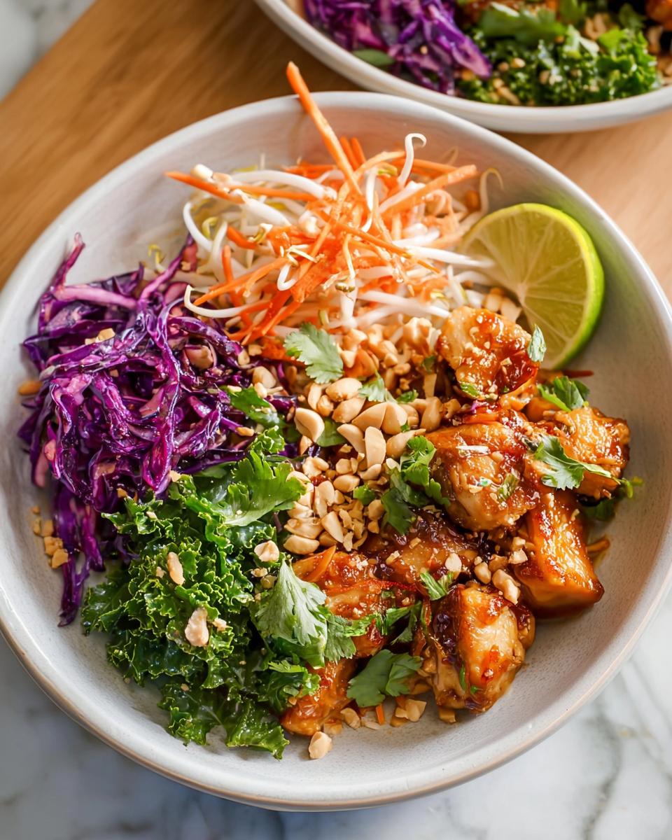 A colorful bowl of Simple Chicken At Home with shredded red cabbage, bean sprouts, carrots, kale, peanuts, and a lime wedge.