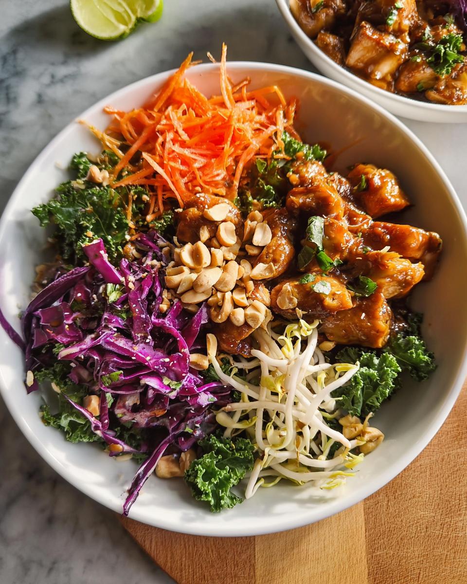 A vibrant bowl of Simple Chicken At Home with shredded carrots, red cabbage, bean sprouts, kale, and peanuts.